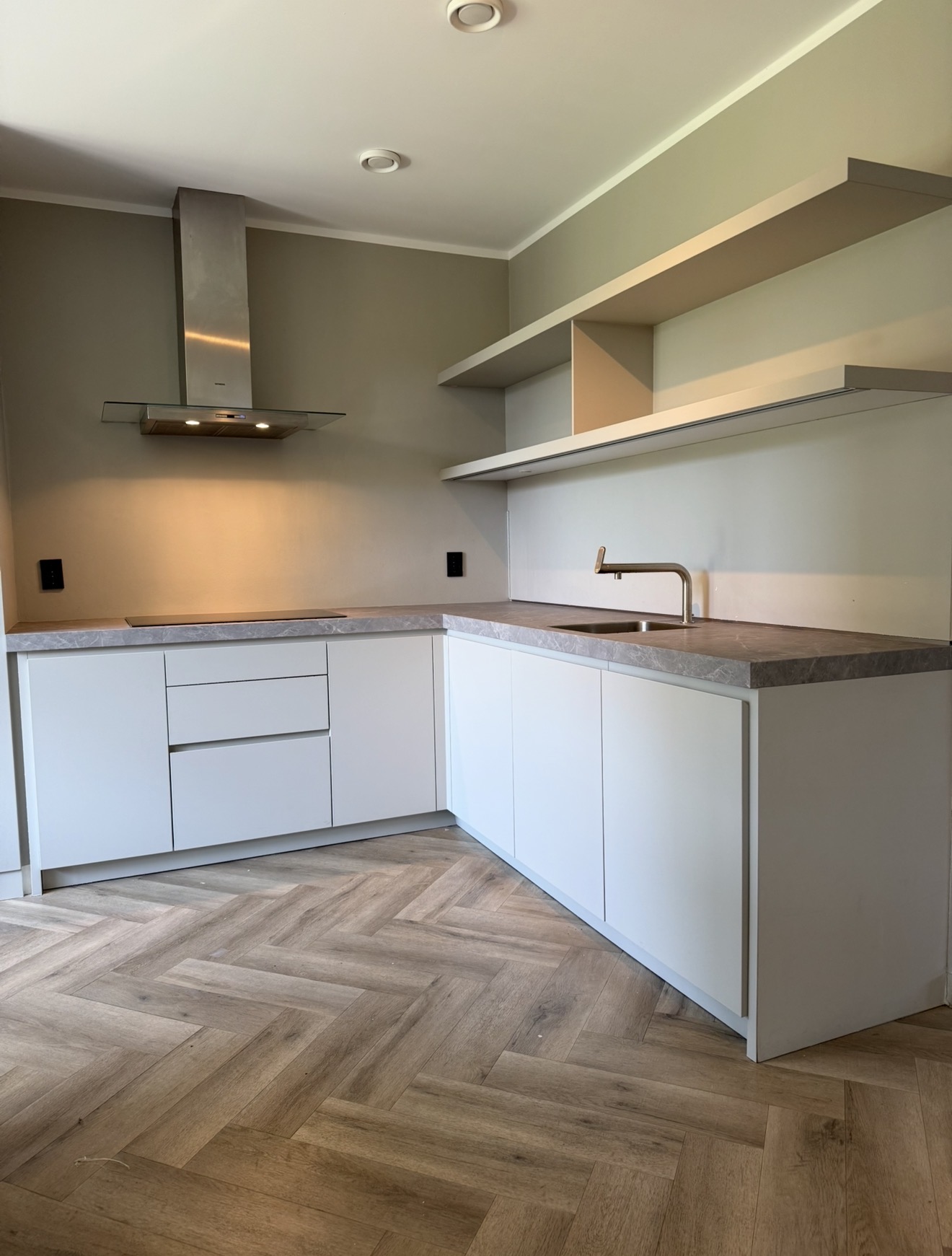 Compacte witte hoekkeuken met een grijs stenen werkblad en open wandvakken