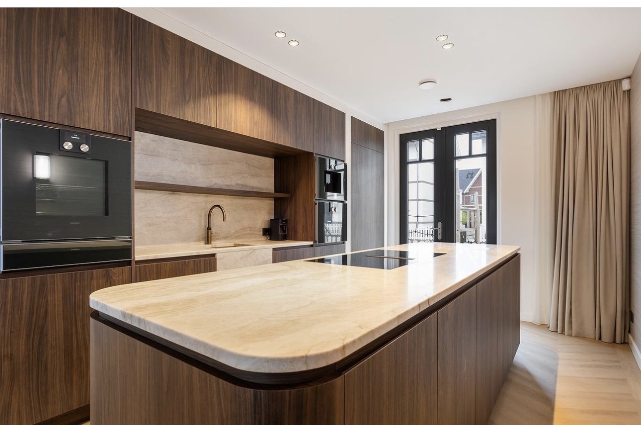 Warme keuken met donkerbruine houtlook fronten en een licht natuurstenen kookeiland
